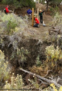 Southwest Conservation Corps co-crew leader Dillon and members Sarah and Aaron complete an H-brace in Spring Creek Basin's southeastern fence line while SJMA's Kathe Hayes offers them chocolate-chip cookies. On their third day of work, the crew is almost to the arroyo at the base of the steep hill.