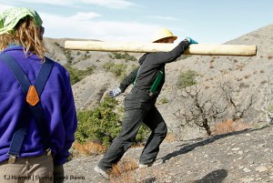 Southwest Conservation Corps member Aaron watches Sarah carry an H-brace post up the steep hill on Spring Creek Basin's southeastern boundary.